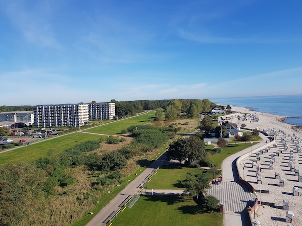 Un complex turístic a la costa, amb una platja, zona d'aparcament i un edifici gran de diverses plantes.