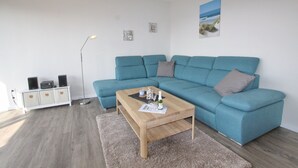 A modern living room with a teal sofa, a wooden coffee table, and a floor lamp. - Haus Baltic App. 177 Inkl. Wlan (Grömitz)