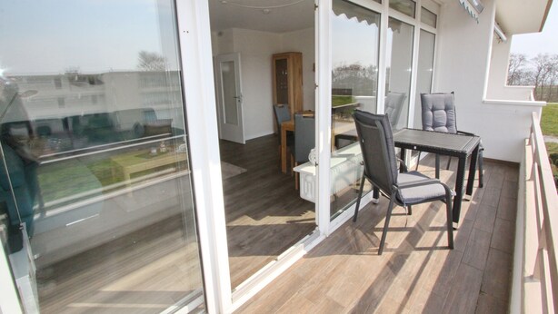 A balcony with a table and chairs, a wooden cabinet, and a glass door leading to an interior space. - Haus Baltic App. 177 Inkl. Wlan (Grömitz)
