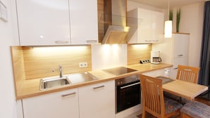 Una cucina moderna con mobili bianchi, un lavello in acciaio inox, forno integrato e piano di lavoro in legno.