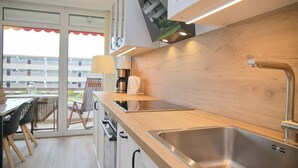 Una cocina moderna con encimera de madera, lavamanos de acero inoxidable y electrodomésticos integrados. Se ve un comedor con mesa y sillas a través de una puerta de vidrio.