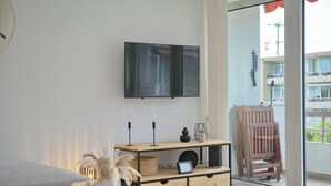 Una sala de estar moderna con una consola de madera, un televisor montado en la pared y un ventanal corredero que da a un balcón exterior.