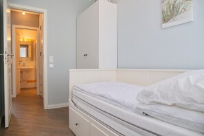 Cozy retreat with a neatly made bed, wardrobe, and bedside table, featuring a door to a bathroom.