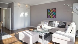 A modern living room with a glass coffee table, a white sofa, and a large painting on the wall. - Miramar App. 707 Inkl. Wlan (Grömitz)