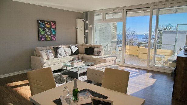 A modern living room with a sofa, coffee table, and dining area. - Miramar App. 707 Inkl. Wlan (Grömitz)