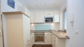 A compact kitchen with white cabinets, a stainless steel oven, and a microwave. - Miramar App. 707 Inkl. Wlan (Grömitz)