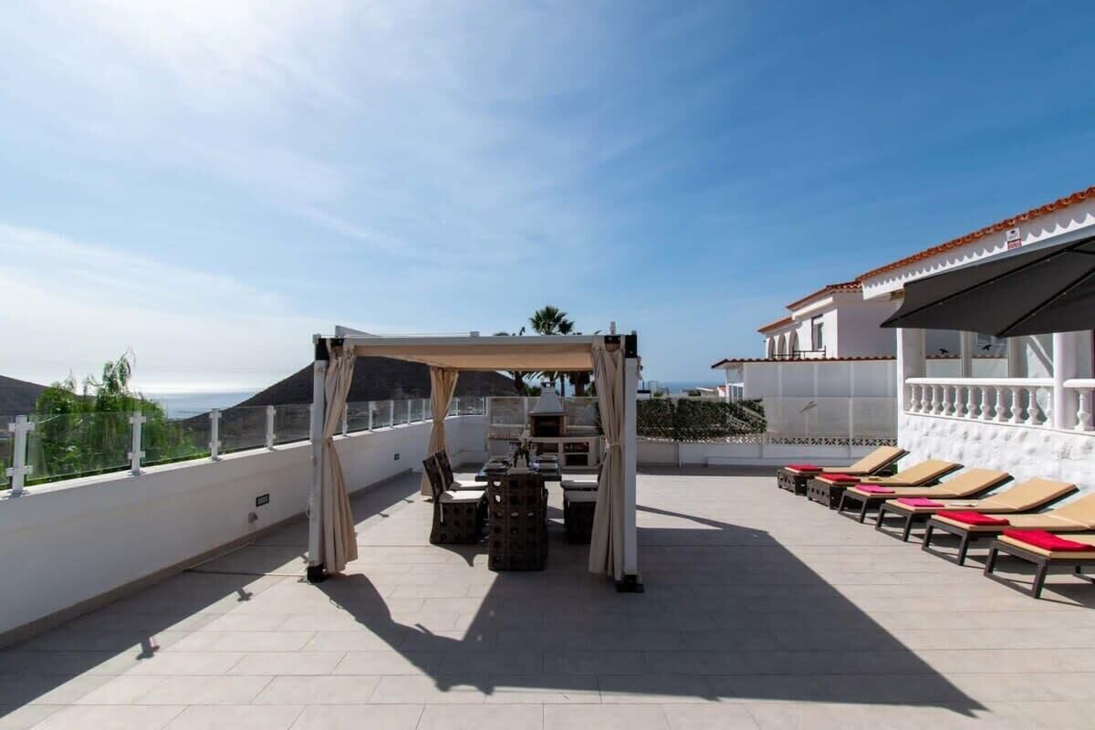 A rooftop terrace with a covered seating area, lounge chairs, and a view of the sea.