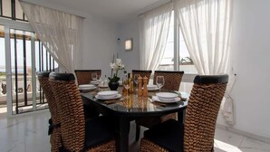 A dining area with a glass table, wicker chairs, white plates, and a vase of flowers. - Villa Melua (Chayofa)