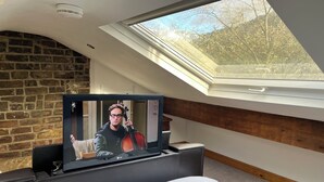 A room with a skylight, a television, a bed with a patterned bedspread, and a brick wall. - Royd Villas,Spacious &Quiet,Log Burner,Patio & TV bed in Centre of Hebden Bridge (Hebden Bridge)