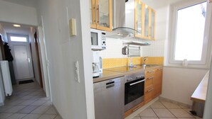 A compact kitchen with a dishwasher, oven, microwave, and wooden cabinets. - Grömitz-center II App. 41 Inkl. Wlan (Grömitz)