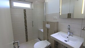 A modern bathroom with a toilet, sink, and shower. - Grömitz-center II App. 41 Inkl. Wlan (Grömitz)
