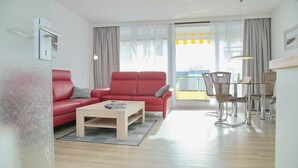 A modern living room with a red sofa, a wooden coffee table, and wicker chairs around a glass table. - Miramar App. 705 Inkl. Wlan (Grömitz)