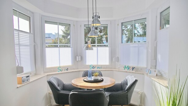 Un coin repas avec une table ronde en bois, quatre chaises noires et des luminaires suspendus.