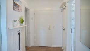 Un couloir avec une porte blanche, une étagère avec des plantes et un porte-manteau suspendu.