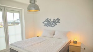 Une chambre à coucher avec un lit, des tables de chevet avec des lampes, une œuvre d’art murale et une fenêtre avec des stores.