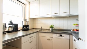 A modern kitchen with white cabinets, a dishwasher, a coffee maker, and a sink. - Miramar App. 503 Inkl. Wlan (Grömitz)