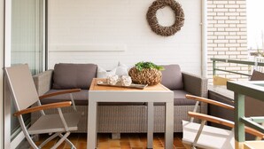A modern outdoor seating area with a white brick wall, a wicker sofa, and a small table with a plant and decorative items. - Miramar App. 503 Inkl. Wlan (Grömitz)