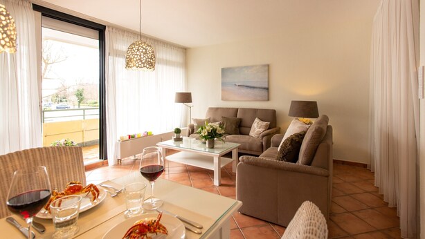 A living room with a dining area, featuring a table set with plates and glasses, a sofa, and a painting on the wall. - Miramar App. 503 Inkl. Wlan (Grömitz)