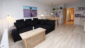 Un salon moderne avec un canapé noir, une table basse en bois et un tableau représentant des champs de lavande accroché au mur.