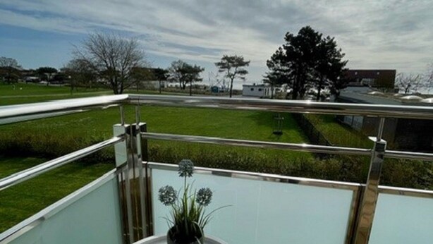 Un balcon doté d’une balustrade en verre, une petite table ronde et une plante en pot.
