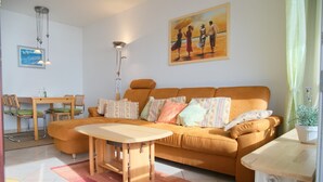 Una sala de estar con un sofá, una mesa de centro de madera, una mesa de comedor con sillas y un cuadro en la pared.