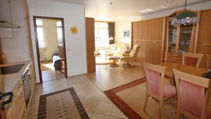 Un vaste espace de vie comprenant un coin repas avec table et chaises, une cuisine équipée de placards et une vue sur l’extérieur.
