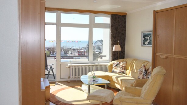Un salon avec un canapé, une table basse et une vue sur la mer grâce à de grandes fenêtres.