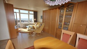 Un vaste salon avec vue sur la mer, un coin repas avec une table jaune et des meubles en bois contenant de la verrerie.