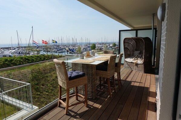A balcony with wicker furniture, a table, and a view of a marina with boats. - Seeblick Seeloft Inkl. Wlan (Grömitz)