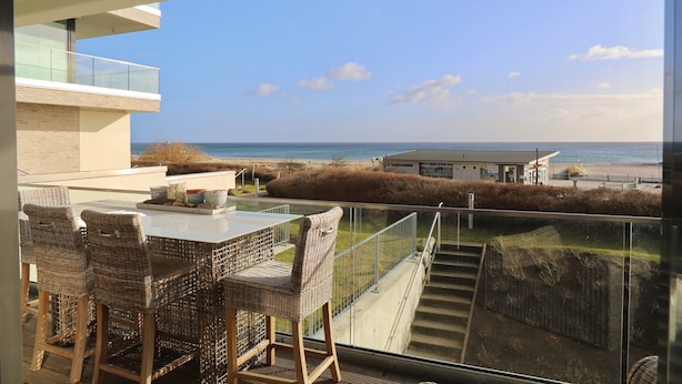A balcony with wicker furniture overlooking a beach and ocean.