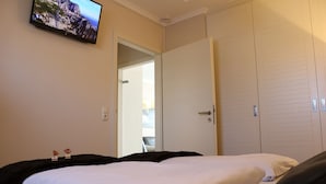 Et hotelværelse med en seng, et fjernsyn ophængt på væggen og en garderobeskab med skydelåger.