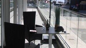 En balkon med to fletstole, et bord, en flaske og en potteplante.