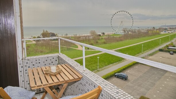 A balcony with a view of a beach, a Ferris wheel, and a parking area. - Hanseat I Appartement. 79 (Grömitz)