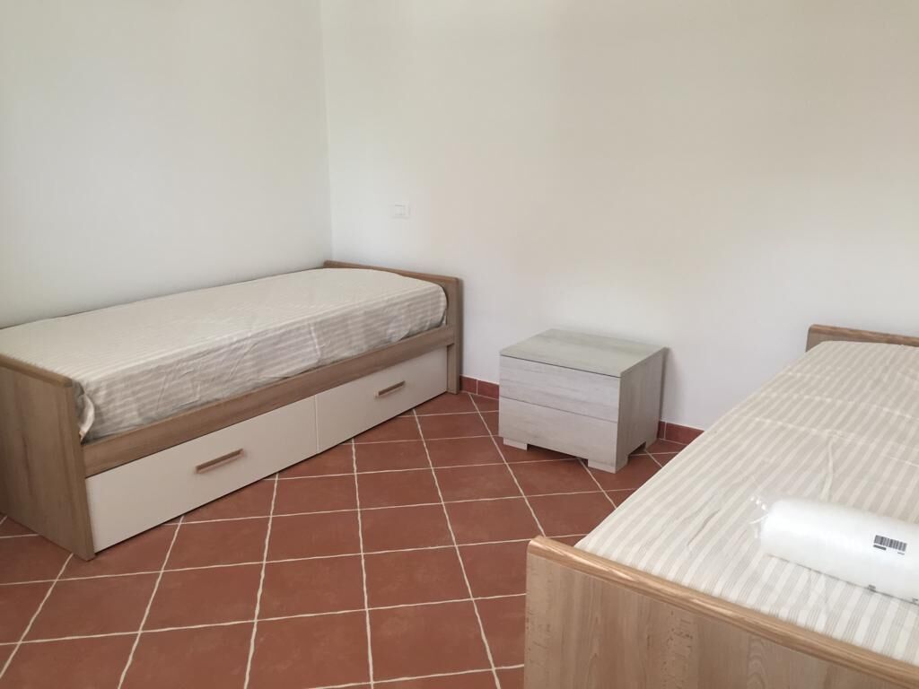 A small, clean room with a single bed, a nightstand, and a small drawer unit.