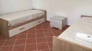 Une petite chambre propre, avec un lit simple, une table de chevet et une petite commode.