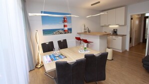 Un espace repas moderne avec une table en bois, des chaises noires et un tableau représentant un phare rouge et blanc accroché au mur.