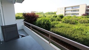 Un balcon avec une table et des chaises, donnant sur un jardin et un immeuble doté de nombreuses fenêtres.