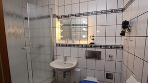 A bathroom with a glass shower enclosure, a sink, a mirror with lights, and a toilet. - Haus Seerose App. 6 Inkl. Wlan (Grömitz)