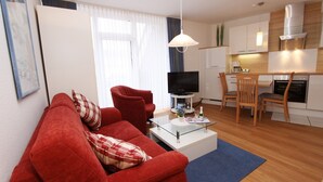 A modern living room with a red sofa, a glass coffee table, and a television. - Haus Seerose App. 6 Inkl. Wlan (Grömitz)