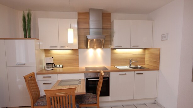A modern kitchen with white cabinets, a wooden countertop, a built-in oven, and a dining area with a wooden table and chairs. - Haus Seerose App. 6 Inkl. Wlan (Grömitz)