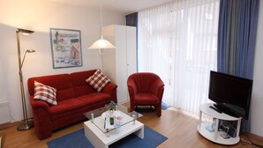 A living room with a red sofa, a red armchair, a glass coffee table, a TV on a stand, and a painting on the wall. - Haus Seerose App. 6 Inkl. Wlan (Grömitz)
