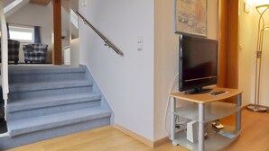 Una escala que condueix a un segon pis, un televisor de pantalla plana sobre un suport i un quadre a la paret.