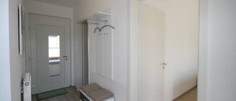 A hallway with a door leading to a room, a small bench, a coat rack, and a mirror on the wall.