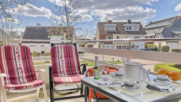 A balcony with two striped chairs, a table set with a bottle, glasses, a teapot, cups, and oranges. - Haus Belvedere App. 1 Inkl. Wlan (Grömitz)