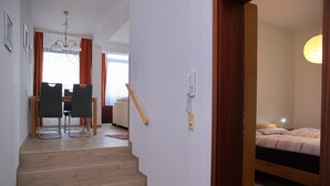 A staircase leading to a bedroom with a bed, a bedside table, and a lamp. There is a wooden chair and a table with chairs in the adjacent room. - Haus Belvedere App. 1 Inkl. Wlan (Grömitz)