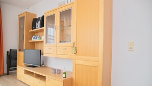 A room with a wooden entertainment unit, a television, and a small table with decorative items. - Haus Belvedere App. 1 Inkl. Wlan (Grömitz)