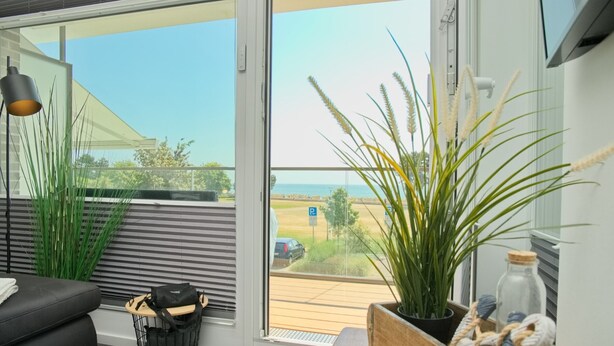 Ein modernes Wohnzimmer mit großem Fenster, einer schwarzen Couch, einem Holztisch und einem Blumentopf.