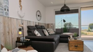 Ein modernes Wohnzimmer mit einem Ecksofa, einer Holzkiste und einem großen Fenster mit Blick.