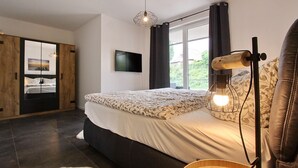 Ein Schlafzimmer mit Bett, Fernseher, Lampe und einem Fenster mit Vorhängen.