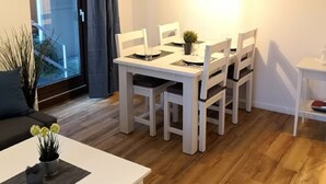 A dining area with a white table and chairs, a hanging pendant light, and a view through a glass door. - Haus Belvedere App. 7 Inkl. Wlan (Grömitz)